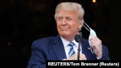 USA, Washington, U.S. President Donald Trump takes off his face mask as he comes out on a White House balcony