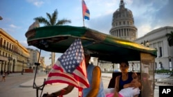 A taxi pedals his bicycle, decorated with Cuban and U.S. flags, as he transports a woman holding a sleeping girl, near the Capitolio in Havana, Cuba, March 15, 2016. 