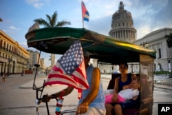 A taxi pedals his bicycle, decorated with Cuban and U.S. flags, as he transports a woman holding a sleeping girl, near the Capitolio in Havana, Cuba, March 15, 2016.