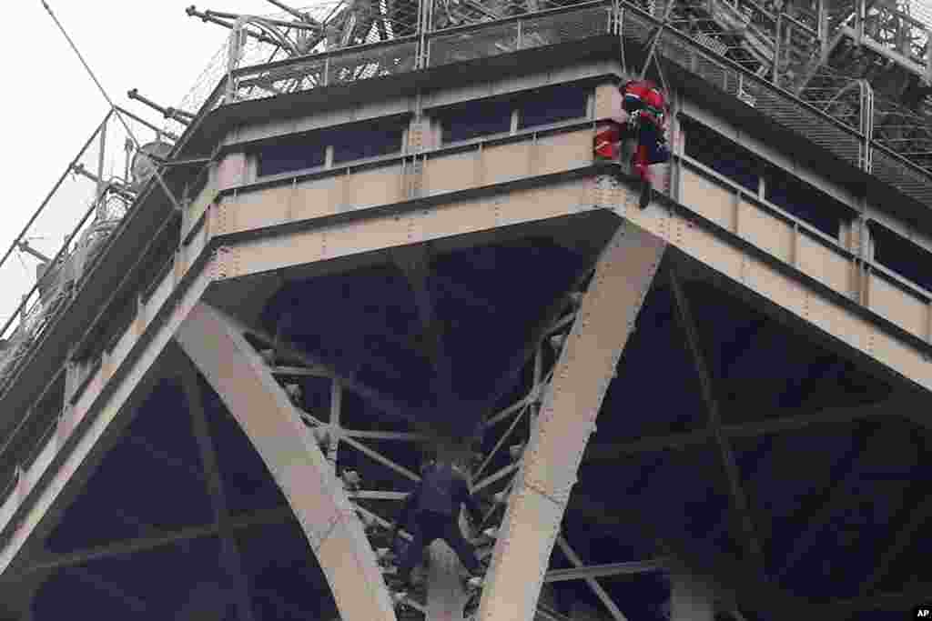 A man climbs the Eiffel Tower in Paris, France as a rescue worker tries to remove him.