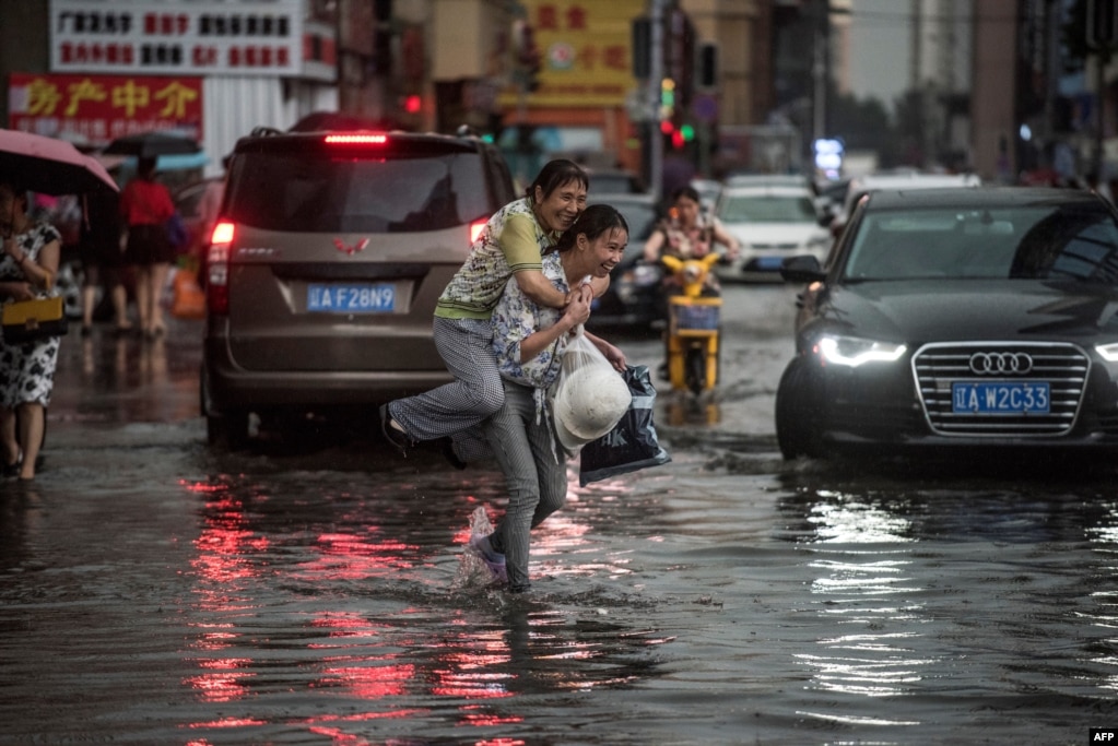 中國沈陽，暴雨過後，一位女子背著上了年紀的婦女趟水過街（2017年7月14日）