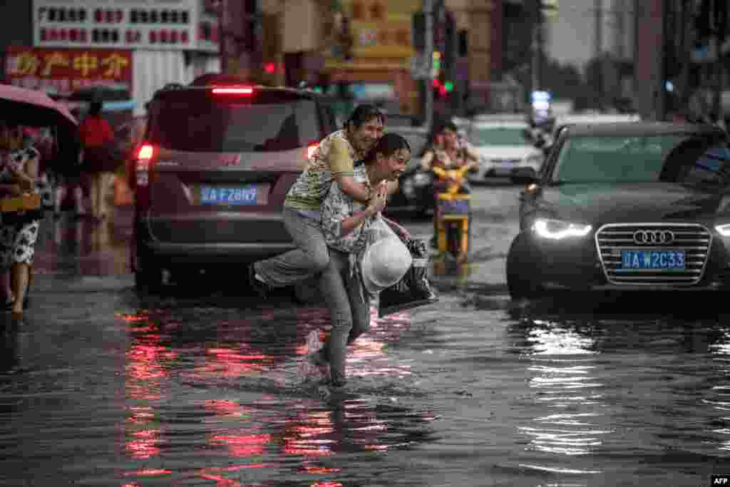 A woman holds an elderly woman on her back to cross a flooded street after a heavy rain in Shenyang, Liaoning province, China.