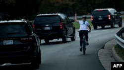 This file photo taken on October 28, 2017 shows a woman on a bike gestures with her middle finger as a motorcade with U.S. President Donald Trump departs Trump National Golf Course in Sterling, Virginia.