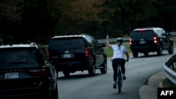This file photo taken on October 28, 2017 shows a woman on a bike gestures with her middle finger as a motorcade with U.S. President Donald Trump departs Trump National Golf Course in Sterling, Virginia.