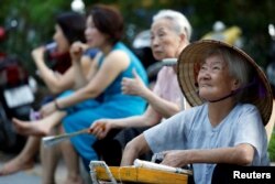 FILE - A cigarette seller, right, waits for customers by Hoan Kiem lake in Hanoi, Vietnam, June 27, 2017.