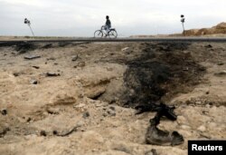 FILE - An Afghan man rides on a bicycle past the site of a car bomb attack where U.S soldiers were killed near Bagram air base, Afghanistan, April 9, 2019.