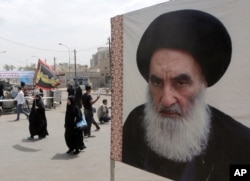 FILE - Shii'te pilgrims make their way to the shrine of Imam Moussa al-Kadhim as passing by a poster of Shi'ite spiritual leader Grand Ayatollah Ali al-Sistani, right, in Baghdad, Iraq.