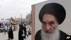 FILE - Shii'te pilgrims make their way to the shrine of Imam Moussa al-Kadhim as passing by a poster of Shi'ite spiritual leader Grand Ayatollah Ali al-Sistani, right, in Baghdad, Iraq.