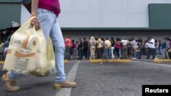 A woman carries bags with toilet paper rolls as people queue to buy staple items at a Makro supermarket in Caracas Aug. 4, 2015.