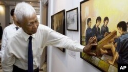 Ông Vann Nath, 1 trong 7 người sống sót ở nhà tù Tuol Sleng, giải thích một bức tranh nói về cách tra tấn trong tù, tại buổi trưng bày tranh của ông ở Phnom Penh 
