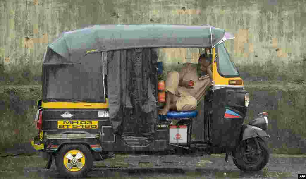 Seorang pengemudi auto-rickshaw, sejenis bajaj di India, menggunakan ponselnya saat istirahat ketika hujan deras melanda Mumbai, India.