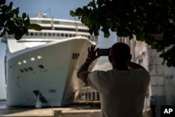 FILE - In this June 17, 2017, photo, a man takes a photo of a cruise ship in Havana harbor, Cuba.
