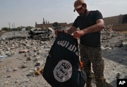 FILE - A fighter of the Christian Syriac militia burns an IS flag on the front line on the western side of Raqqa, northeast Syria, July 17, 2017.