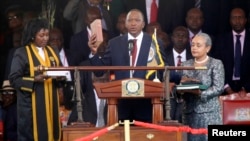 Kenya's President Uhuru Kenyatta takes the oath of office as his wife Margaret holds a bible during the official swearing-in ceremony at Kasarani Stadium in Nairobi, April 9, 2013. 