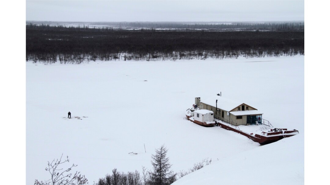 Seorang nelayan mengangkut tangkapannya dari lubang di es dekat tongkang penelitian Stasiun Sains Timur Laut dekat Chersky, Rusia. (Foto: AP/Arthur Max)