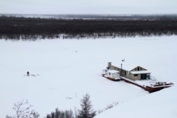 Seorang nelayan mengangkut tangkapannya dari lubang di es dekat tongkang penelitian Stasiun Sains Timur Laut dekat Chersky, Rusia. (Foto: AP/Arthur Max)