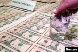 A police officer immerses a counterfeit U.S. dollar bill in liquid to show its quality during a media conference in Lima April 17, 2013. (FILE PHOTO/REUTERS)