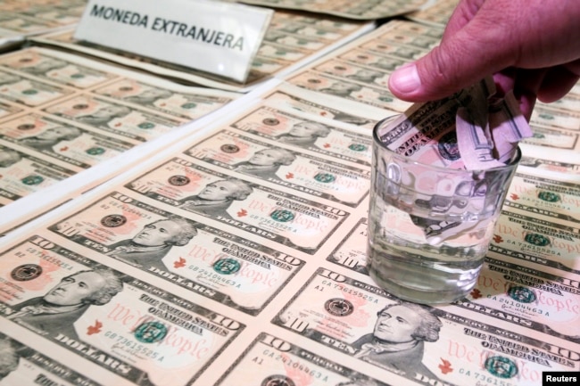 A police officer immerses a counterfeit U.S. dollar bill in liquid to show its quality during a media conference in Lima April 17, 2013. (FILE PHOTO/REUTERS)