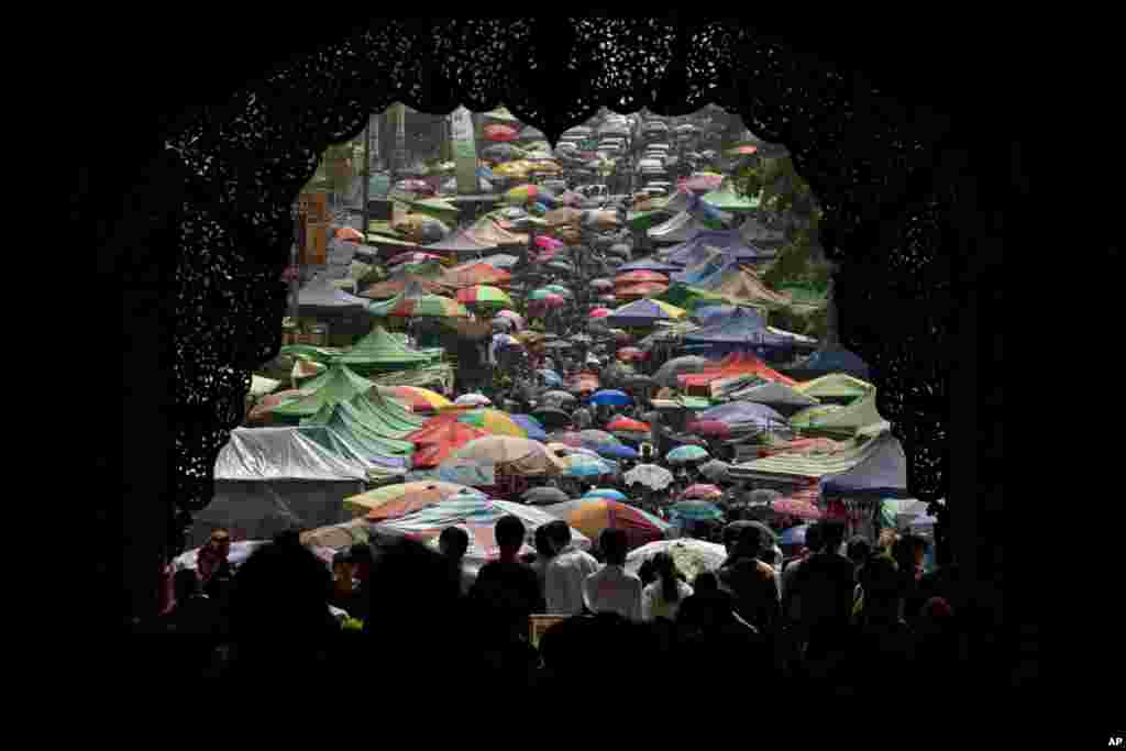 Buddhist devotees walk with umbrellas through the temporary tents of souvenir shops on a road leading to an entrance to Shwedagon pagoda in Yangon, Myanmar, Thursday, April 17, 2014. Myanmar Buddhists concluded celebrating their annual water festival, kno