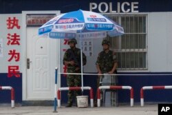 FILE - Chinese paramilitary police stand on duty in front of a wanted poster in the city of Aksu in western China's Xinjiang province, July 17, 2014. China has blanketed parts of Xinjiang, home to Muslim, Turkic-speaking Uighurs, with heavy security.