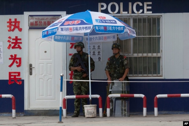 FILE - Chinese paramilitary police stand on duty in front of a wanted poster in the city of Aksu in western China's Xinjiang province, July 17, 2014. China has blanketed parts of Xinjiang, home to Muslim, Turkic-speaking Uighurs, with heavy security.