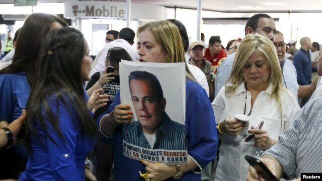 Una mujer sostiene una foto de Manuel Rosales junto a la esposa de Rosales, Eveling Trejo de Rosales, mientras aguardaban su llegada al aeropuerto de Maracaibo, Venezuela, el jueves 15 de octubre de 2015.