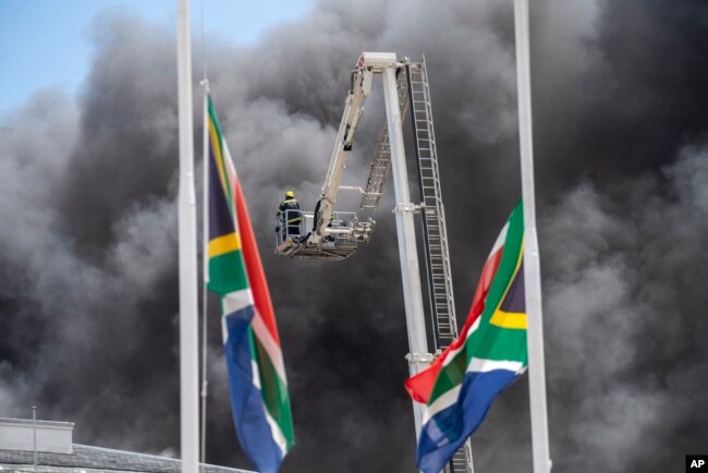 Firemen spray water on flames erupting from a building at South Africa's Parliament in Cape Town Sunday Jan. 2, 2022.