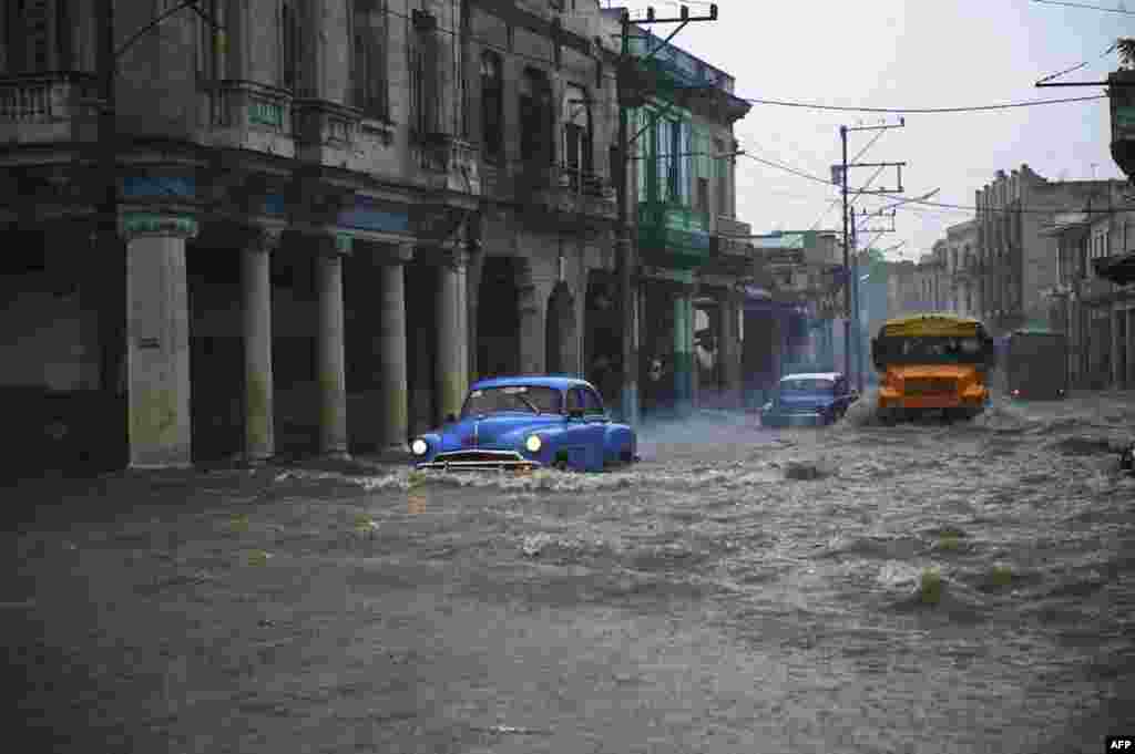 Old American cars and buses drive through a flooded street in Havana, Cuba, June 30, 2021.