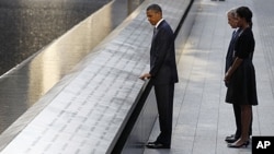 President Barack Obama touches the names of victims engraved on the side of the north pool of the World Trade Center site as former President George W. Bush, first lady Michelle Obama and former first lady Laura Bush (obscured) look on during ceremonies m