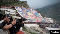 Tibetan Buddhists, tourists view a huge Thangka, a religious silk embroidery or painting displaying a Buddha portrait, during the Shoton Festival at Zhaibung Monastery in Lhasa, capital of southwest China's Tibet Autonomous Region, Aug. 25, 2014.