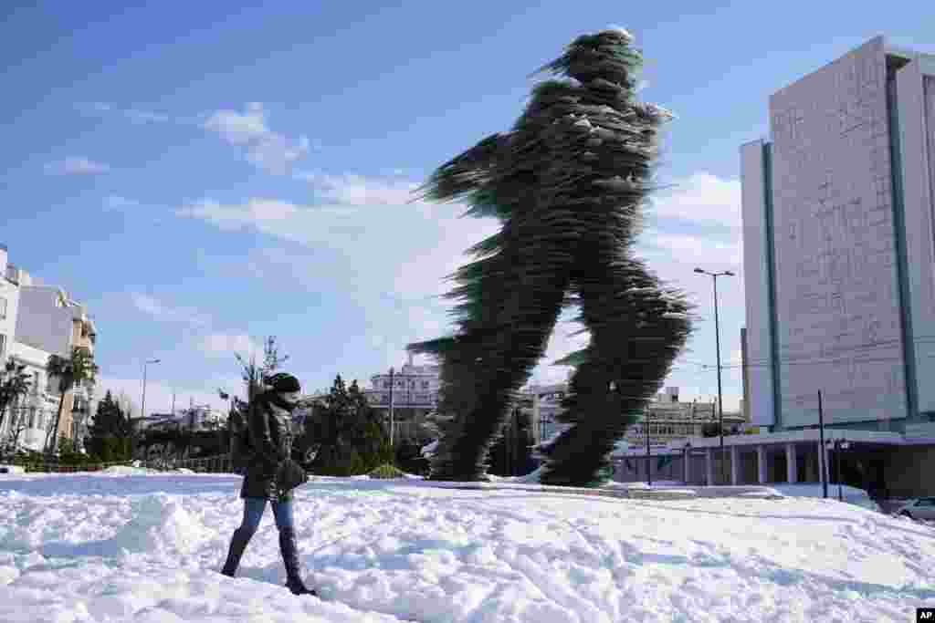 A woman walks past a the Runner, sculptured by Kostas Varotsos, after a snowstorm, in Athens, Greece.