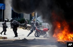A Venezuelan Bolivarian National police officer drops a privately owned motorcycle into the flames after an explosion at Altamira square during clashes against anti-government demonstrators in Caracas, Venezuela, Sunday, July 30, 2017.