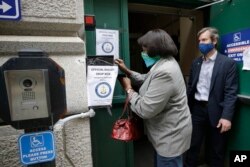 FILE - A voter, left, places a ballot in a secure box as Providence City Clerk Shawn Selleck, right, looks on, Tuesday, June 2, 2020, in Providence, R.I. More American voters asked for mail ballots during the coronavirus outbreak.