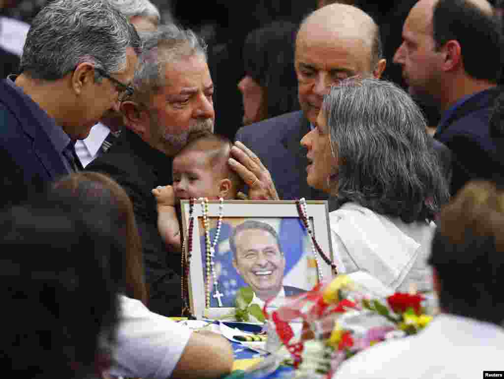 O cantor Caetano Veloso ao lado do ex-Presidente brasileiro, Luiz Inácio Lula da Silva, que segura o bebé do candidato presidencial Eduardo Campos, enquanto fala com a sua viúva Renata, durante o velório no Palácio do Governo de Pernambuco no Recife. O líder do Partido Socialista, Eduardo Campos, de 49 anos, morreu num acidente de avião a 13 de Agosto. Agosto 17, 2014