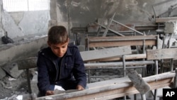 FILE - A boy reads a torn paper inside a classroom in his destroyed school in Aleppo, Syria.