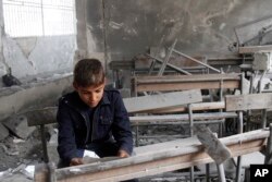 FILE - A boy reads a torn paper inside a classroom in his destroyed school in Aleppo, Syria.