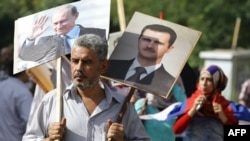 一名叙利亚男子手持叙利亚总统阿萨德和俄罗斯总统普京的肖像，和几百人聚集在俄罗斯驻大马士革大使馆，对俄罗斯的军事行动表示支持（2015年10月13日）。