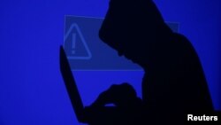 FILE - A hooded man holds a laptop computer as blue screen with an exclamation mark is projected on him in this illustration picture taken on May 13, 2017.