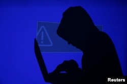 FILE - A hooded man holds a laptop computer as blue screen with an exclamation mark is projected on him in this illustration picture taken on May 13, 2017.