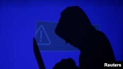 FILE - A hooded man holds a laptop computer as blue screen with an exclamation mark is projected on him in this illustration picture taken on May 13, 2017.