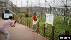 A woman poses for photographs in front of a barbed-wire fence near the demilitarized zone separating the two Koreas in Paju, South Korea, July 14, 2017.