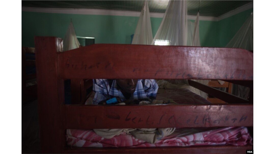 A former Al-Shabab member texts on his phone while lying on his bed in a dormitory at a rehabilitation center for former militants in Baidoa, Somalia, Sept. 17, 2016. (Photo: J. Patinkin/VOA)