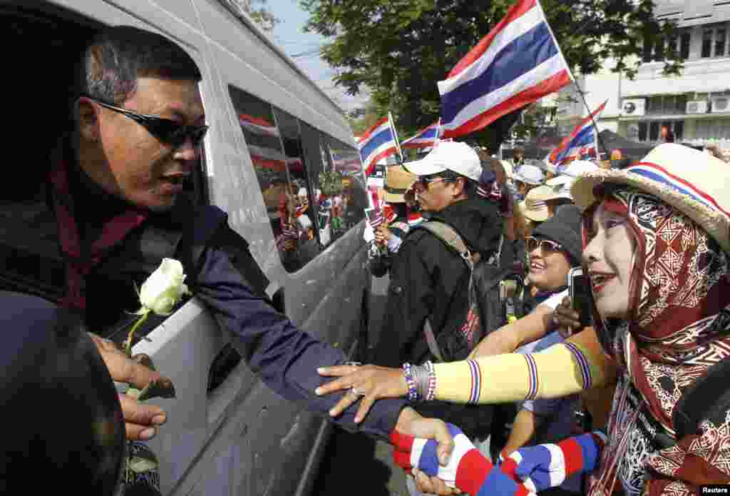 Anti-government protesters give flowers to a Thai border policeman as he leaves the Government House following an agreement between the army and protesters, Bangkok, Thailand, Jan. 19, 2014. 