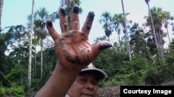 A local resident shows the oil residue left behind along an Amazon tributary from a pipeline. (Credit: International Wow Company)