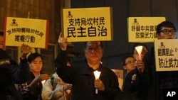 A protester, center, holds up a placard reading: "Supporting Wukan villagers, democracy autonomy" during a candlelight vigil outside the China Liaison Office in Hong Kong to support the Wukan villagers, December 20, 2011.
