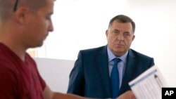 In this photo taken Oct. 7, 2018, President of the Republic of Srpska Milorad Dodik, right, waits at a polling station in the Bosnian town of Laktasi, northwest of Sarajevo, Bosnia.