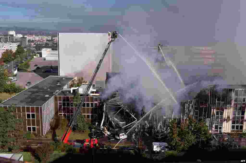 Firefighters stand on ladders spraying liquid from hoses as they attempt to control a factory fire in Villeurbanne, central-eastern France.