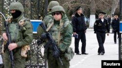 Armed men (L), believed to be Russian servicemen, stand guard outside Ukraine's naval headquarters after it was taken over by pro-Russian forces, as Russian naval officers (R) are seen in the background, in Sevastopol, March 19, 2014.