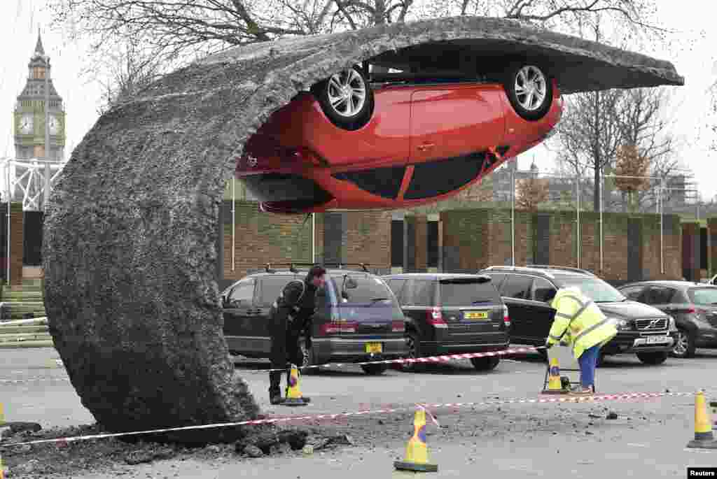 Workers move bollards near an upside-down car art installation by British artist Alex Chinneck in a car park on the South Bank in London.