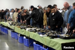 FILE - People look over a table of handguns for sale at a gun show in Kansas City, Missouri, Dec. 22, 2012.